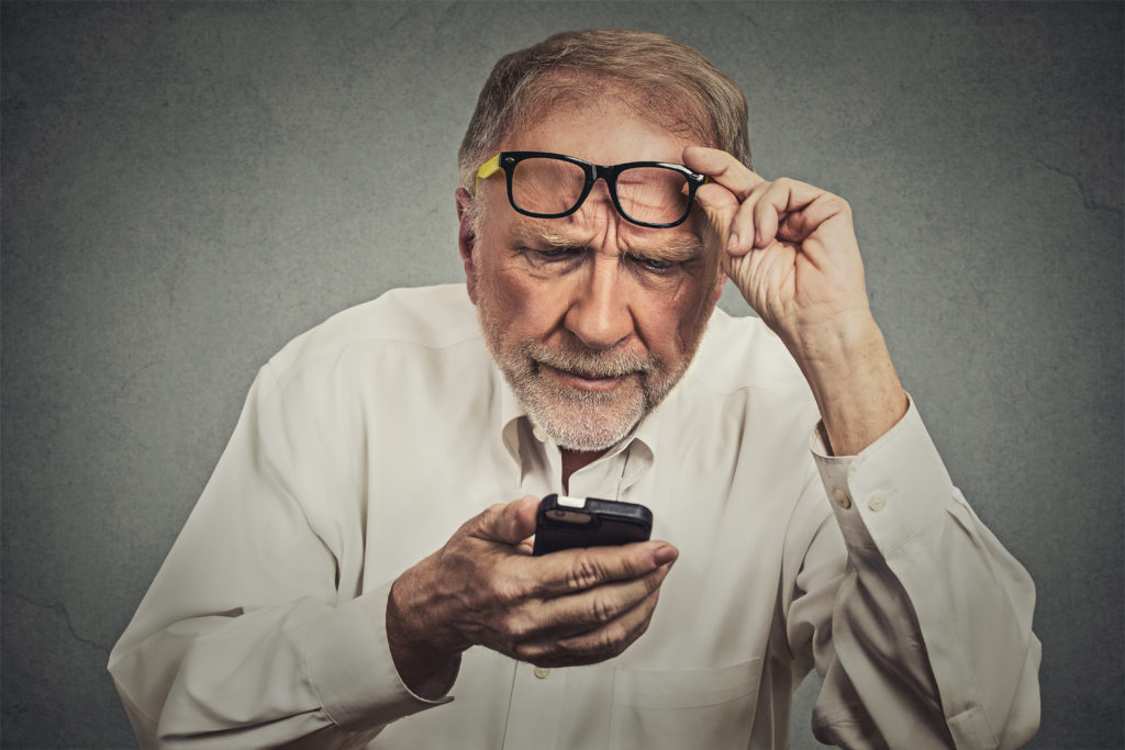 Closeup portrait headshot elderly man with glasses having trouble seeing cell phone has vision problems. Bad text message. Negative human emotion facial expression perception. Confusing technology